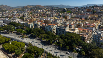 Aerial view of the historic center of Reggio Calabria, Italy. In the foreground is the tree-lined promenade of the city. It is a sunny summer morning.