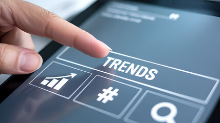 Finger pressing trends button on digital tablet screen with icons for graph hashtag and search in background