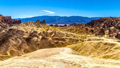 Eroded badlands with layered formations under bright sky, distant mountains