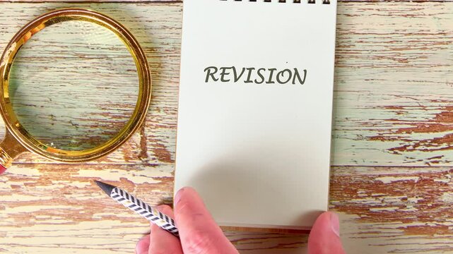 On a wooden table, someone writes strange symbols, then the word REVISION on a small notebook. A golden magnifying glass and patterned pen sit nearby, offering a scholarly atmosphere