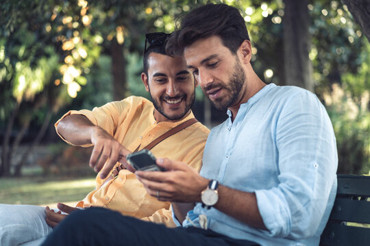 Two friends sharing content on a smartphone while sitting together outdoors