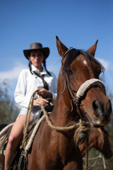 Obraz premium Cowgirl with her horse standing in a green meadow under a blue sky 