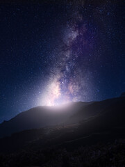Stunning Milky Way galaxy rising over a dark mountain silhouette with glowing light at the horizon.