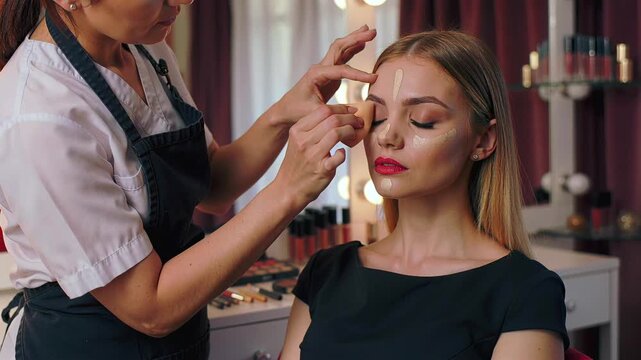 Studio makeup session with model professional makeup artist applies foundation - contours cheekbones - blends eyeshadow - highlights brow bone and finishes bold red lipstick - using brushes