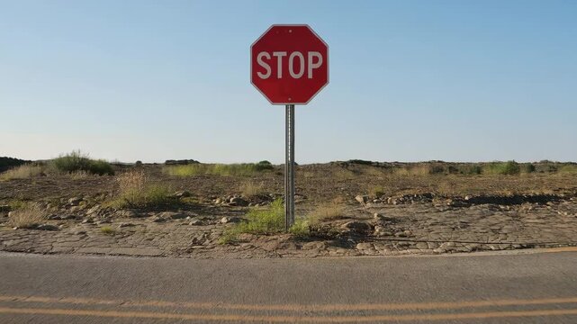 Stop sign at end of paved road facing undeveloped terrain