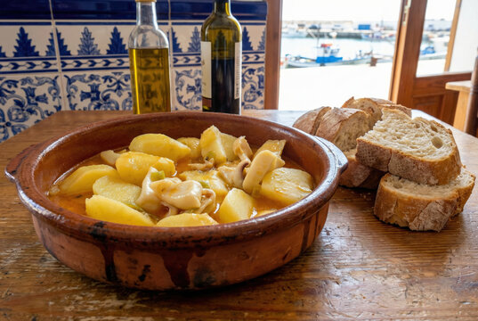 Guiso tradicional de patatas con chocos servido en una cazuela de barro sobre una mesa de madera con pan artesano, aceite de oliva y vino, en un ambiente marinero