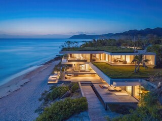 Fototapeta premium Modern beachfront villa with large windows and a green roof. The property overlooks the ocean at dusk, showcasing luxury real estate in a serene environment.