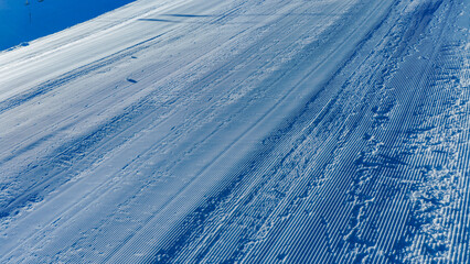 Abstract aerial view of groomed snow surface with visible tracks and patterns, suitable for winter sports backgrounds, alpine concepts, and seasonal design projects