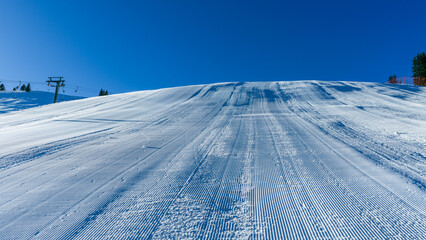 Groomed ski slope captured at an angle, showing textured snow surface and ski tracks, ideal for alpine sports, winter tourism, and resort marketing visuals
