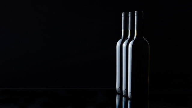 Three wine bottles without labels on a black background