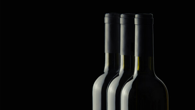 Three wine bottles without labels on a black background