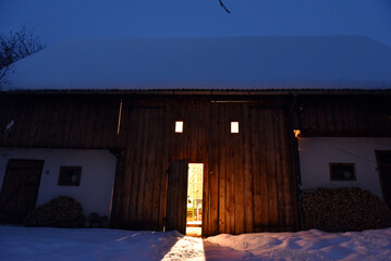 Blue hour snow covered wooden barn with warm light in winter © salajean