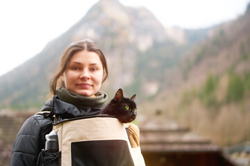 Young woman hiking with black cat in backpack carrier in mountain valley