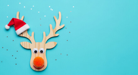 Naklejka premium Wooden reindeer with a red hat on turquoise background with small stars, showing the spirit of Christmas, winter holiday and festive mood for decoration