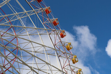 Colorful Ferris wheel gondolas against bright blue sky and clouds.
