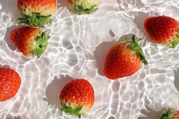 Fresh red strawberries floating in clear water with sunlight shadows.