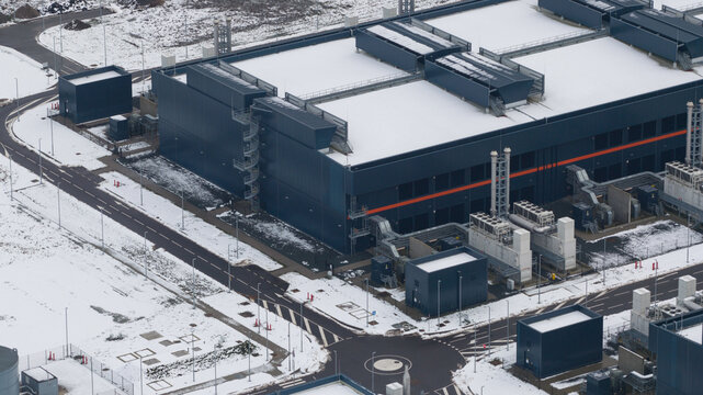 Aerial view of a large, modern datacenter complex dusted with snow, contrasting with the dark metal structures against the white landscape, Middenmeer, North Holland, Netherlands.