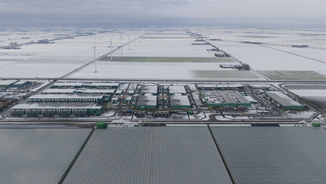 Aerial view of snow-dusted rooftops and fields create a stark contrast against the muted winter landscape, Datacenter Middenmeer, North Holland, Netherlands.