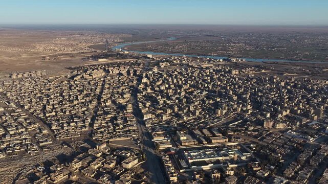 Drone shot overlooking the city of Deir ez-Zor in eastern Syria. The footage captures the urban landscape, traditional architecture, and the strategic flow of the Euphrates River.