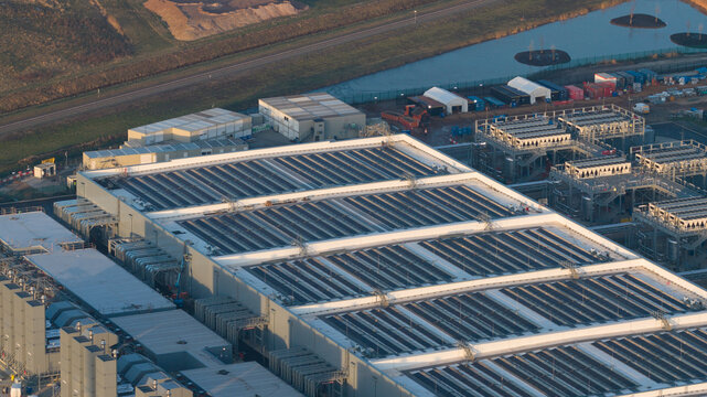 Aerial view of the Google datacenter, a vast expanse of metallic structures reflecting the sunlight, contrasting with the surrounding earthy tones of the landscape, Winschoten, Groningen, Netherlands.