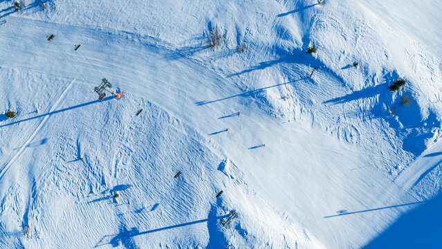 Top down aerial view of alpine ski slopes with skiers, long shadows, and textured snow surface, illustrating winter sports activity and resort infrastructure