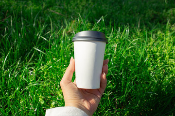 Hand holding paper cup on green grass background outdoors