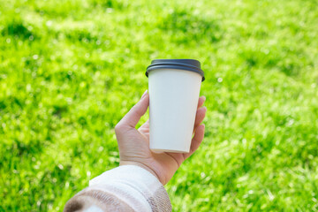 Hand holding paper cup on green grass background outdoors