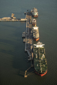 Aerial view of tankers moored at a pier, their hulls reflecting the somber sky above the calm, dark waters, Corpus Christi, United States.