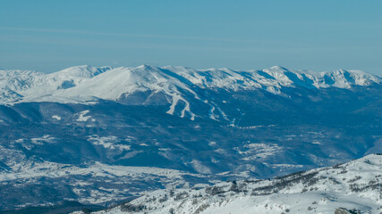 Obraz premium Distant view of Bjelašnica mountain with visible ski slopes and winter terrain, illustrating alpine skiing infrastructure within a rugged mountain environment