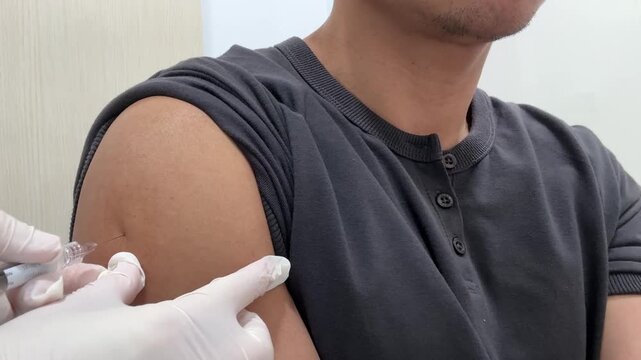 Close-up of Healthcare Professional Administering Vaccination Injection to a Man's Arm, A high-angle, close-up shot of a male patient in a grey shirt receiving a medical injection or vaccine.