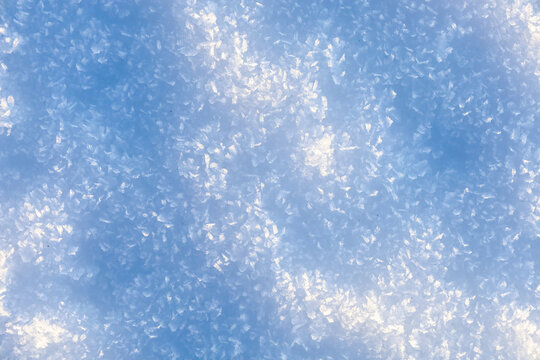 Macro photograph of a sparkling snow surface covered with small ice crystals and delicate frost. The combination of bright white highlights and deep blue shadows creates a cold winter texture with hig