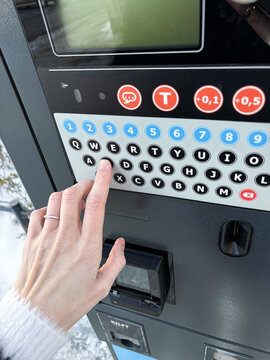 Close-up of a person's hand pressing a button on a parking meter terminal to pay for car parking