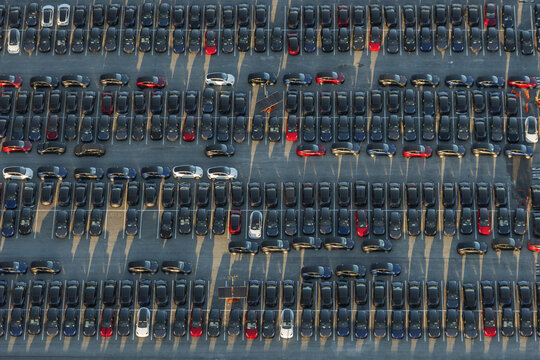 Aerial view of a vast grid of parked cars, an ocean of black and grey punctuated by splashes of red and white, Fremont, United States.