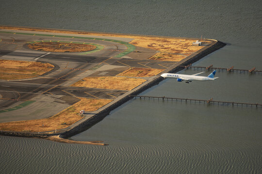 San Francisco, United States - 24 June 2024: Aerial view of an airplane soaring above the runway at San Francisco International Airport, juxtaposed against the calm, rippled waters of the bay.
