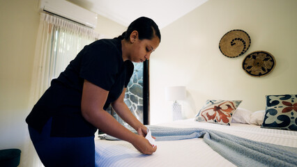 Housekeeper arranging a throw blanket and towel on a clean bed in a tropical resort or hotel room, providing hospitality service