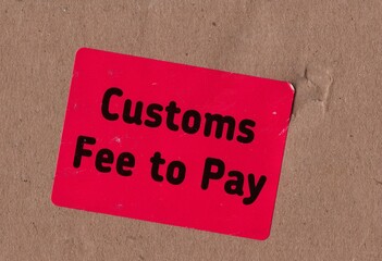 A red CUSTOMS FEE TO PAY sticker on brown packing board.