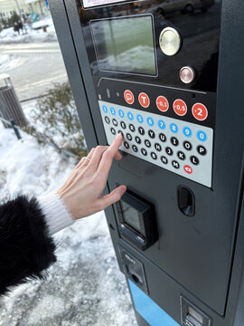 Close-up of a woman's hand using a parking meter to pay for car parking on a city street