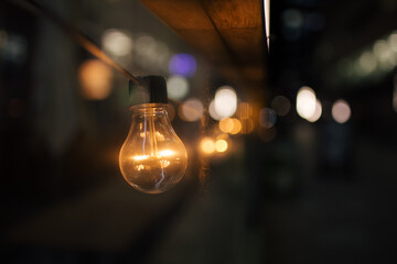 Warm incandescent light bulb glowing on a night street with blurred city lights and bokeh