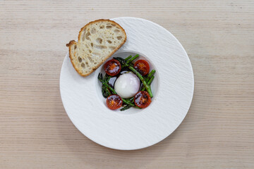A plate of asparagus, tomato, and egg with bread on the side.