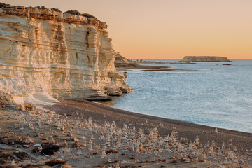 Sunset over a chalk cliff coastline with a pebble beach and rock cairns along the shore, Cyprus
