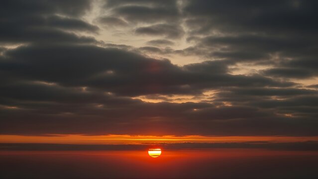 A beautiful dramatic sunset over the sea and lake horizon features a colorful orange and red sky with summer clouds at dusk for a stunning nature landscape