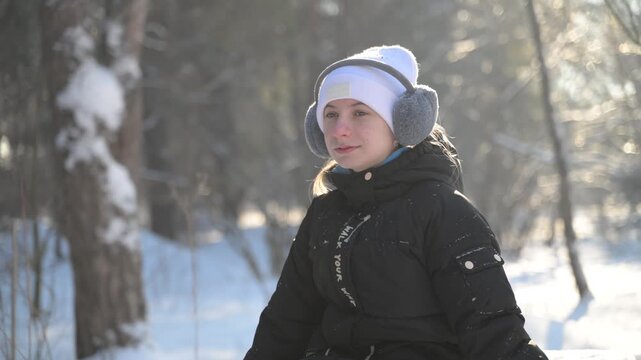 Close-up of a little girl sitting in the snow and exhaling warm breath vapor against a bright sunny winter forest background.