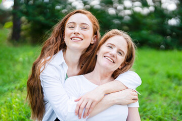 Fototapeta premium Two women smile and enjoy time together in a green park on a sunny day while sitting on grass