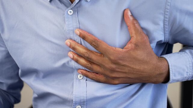 Close up. African american male hands holding massaging chest. Businessman has a heart attack while sitting at a workplace in a business office. Sick black man is breathing deeply, needs medical help