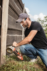 A man with a powerful tool with an angle grinder cleans the wood of the fence - grinding the boards with a coarse grinder brush
