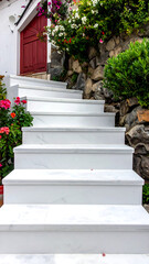 Marble steps lead up to a red door, framed by lush greenery and colorful flowers on a rocky hillside