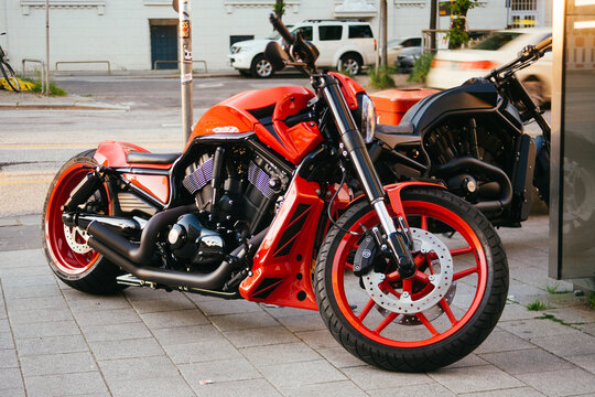 Two sport motorcycles parked on a city sidewalk, a striking red bike in the foreground with a black bike behind