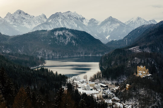 Snowy alpine valley with a lake, forest and a hillside castle against snow-capped mountains