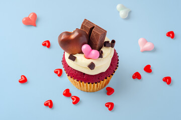 Red velvet cupcake decorated with heart chocolate and heap of red hearts on blue background, valentines day, celebrating love concept