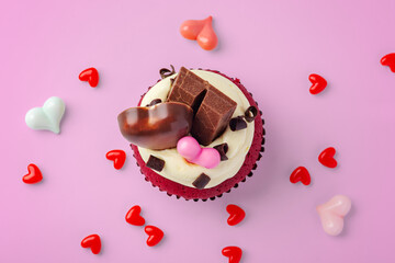 Red velvet cupcake decorated with heart chocolate and heap of hearts on pink background, valentines day, celebrating love concept
